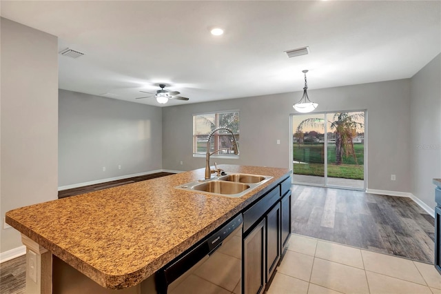 kitchen featuring light wood-type flooring, decorative light fixtures, sink, stainless steel dishwasher, and a kitchen island with sink