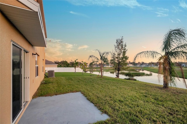 yard at dusk with a water view, cooling unit, and a patio area