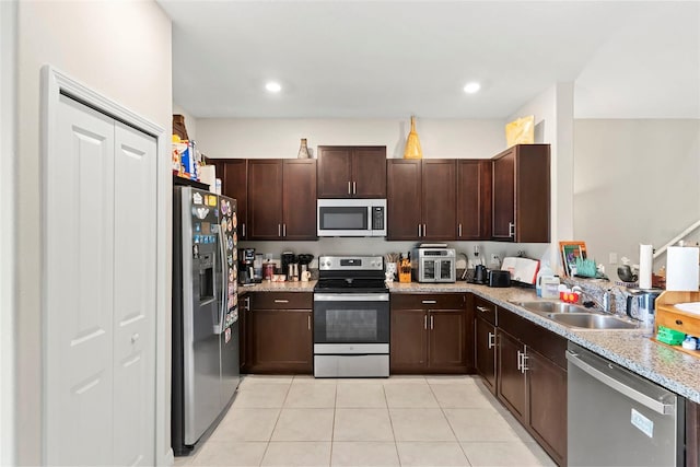 kitchen featuring dark brown cabinetry, sink, light tile patterned floors, light stone countertops, and appliances with stainless steel finishes