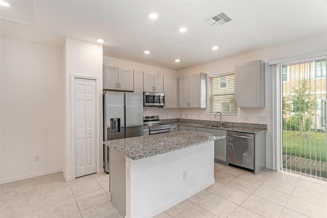 kitchen with a wealth of natural light, appliances with stainless steel finishes, light stone counters, and a kitchen island