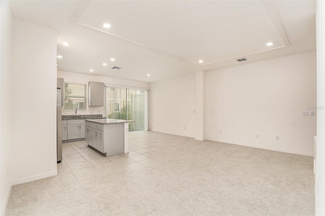 kitchen featuring stainless steel refrigerator, light stone countertops, light tile patterned floors, a center island, and gray cabinetry