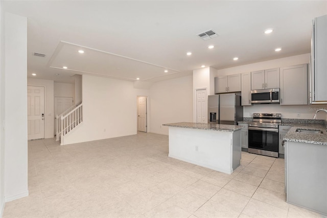 kitchen with stainless steel appliances, sink, light stone counters, a center island, and gray cabinetry