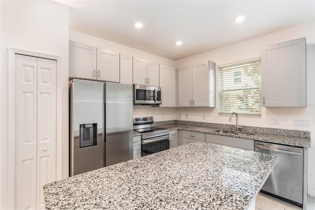 kitchen with stainless steel appliances, sink, light stone counters, and a kitchen island