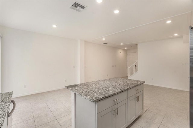 kitchen featuring light tile patterned flooring, light stone countertops, gray cabinetry, and a kitchen island