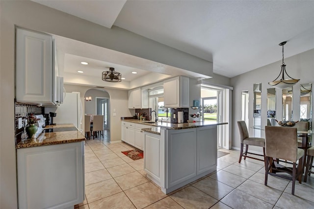 kitchen featuring dark stone counters, white cabinets, hanging light fixtures, sink, and kitchen peninsula