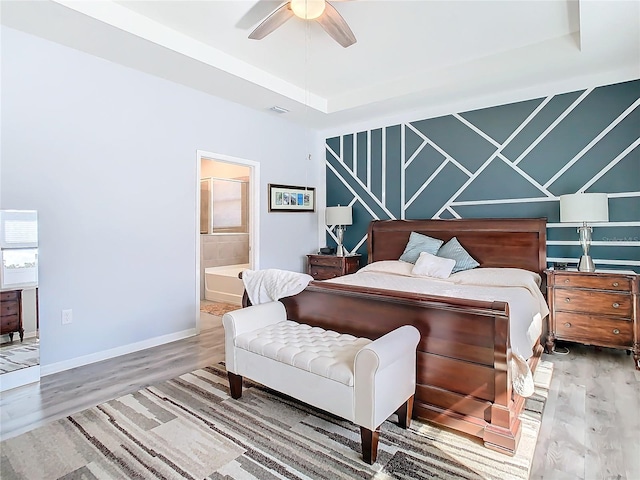 bedroom with a tray ceiling, connected bathroom, ceiling fan, and wood-type flooring