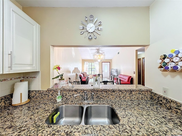 kitchen with stone counters, decorative backsplash, sink, and a chandelier