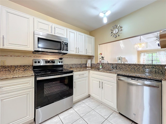 kitchen featuring white cabinetry, sink, dark stone counters, a chandelier, and appliances with stainless steel finishes