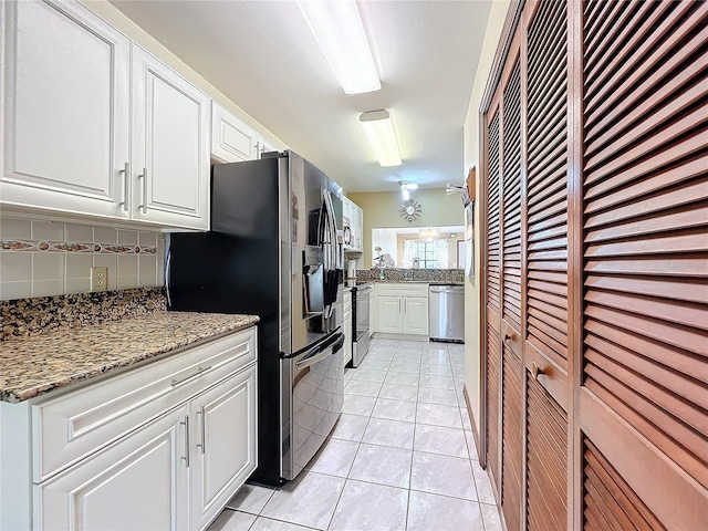 kitchen with appliances with stainless steel finishes, tasteful backsplash, light tile patterned flooring, light stone counters, and white cabinetry