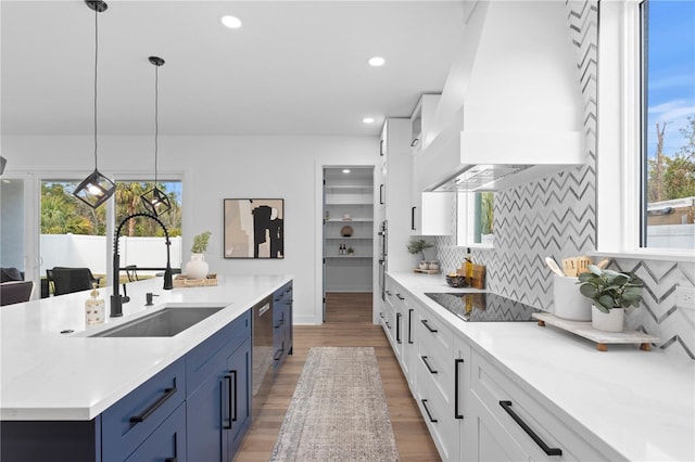 kitchen with black electric stovetop, premium range hood, a sink, blue cabinetry, and pendant lighting