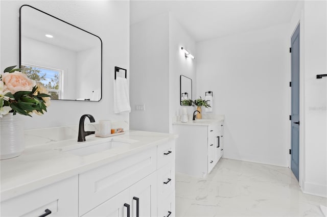 bathroom with marble finish floor, two vanities, and a sink