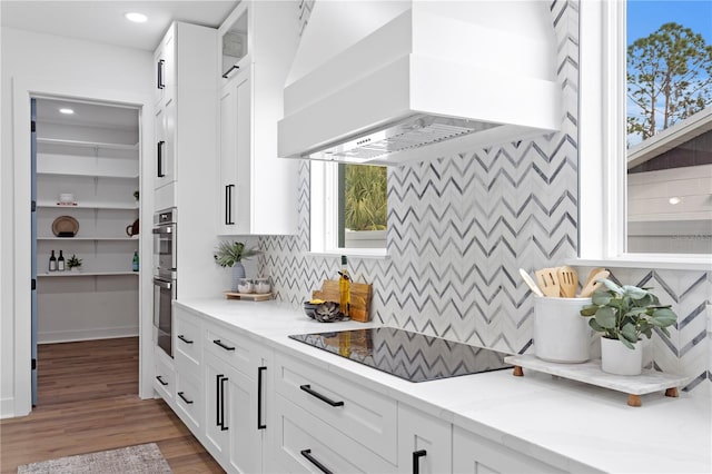 kitchen with light stone countertops, black electric cooktop, white cabinetry, and ventilation hood