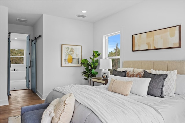 bedroom with wood finished floors, visible vents, multiple windows, and a barn door