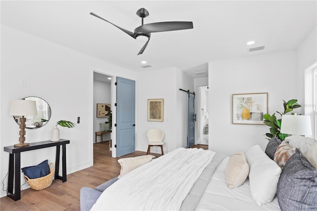 bedroom with light wood finished floors, a barn door, visible vents, and recessed lighting