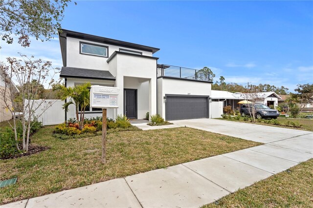 contemporary house with driveway, a garage, a balcony, fence, and a front lawn