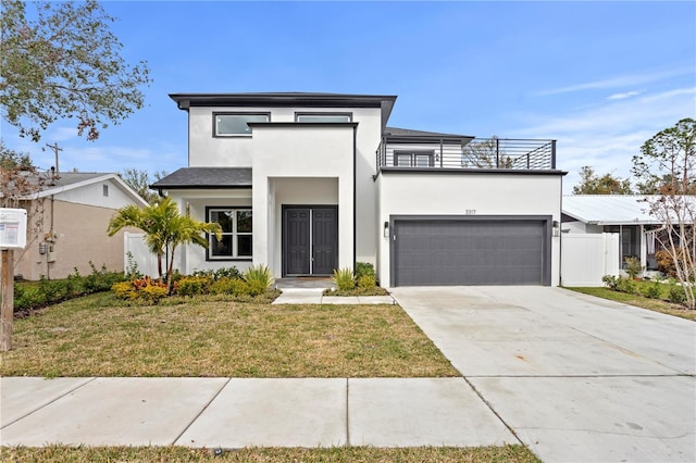 contemporary house with a balcony, a front yard, concrete driveway, and stucco siding