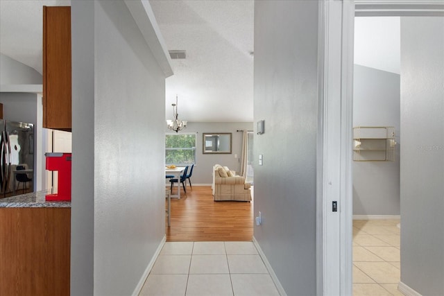 hallway with light tile patterned flooring, lofted ceiling, a textured ceiling, and a chandelier