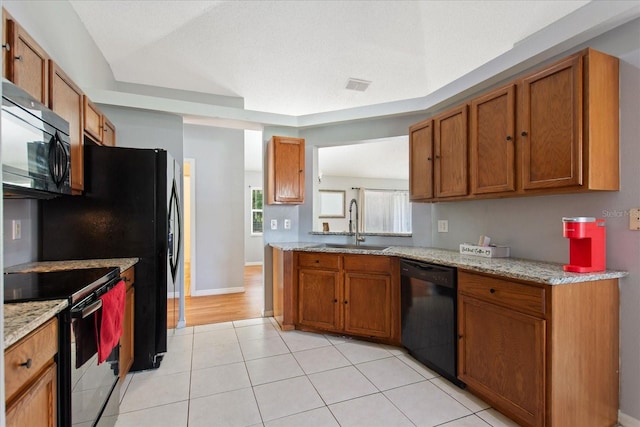 kitchen featuring light tile patterned flooring, sink, light stone countertops, and black appliances