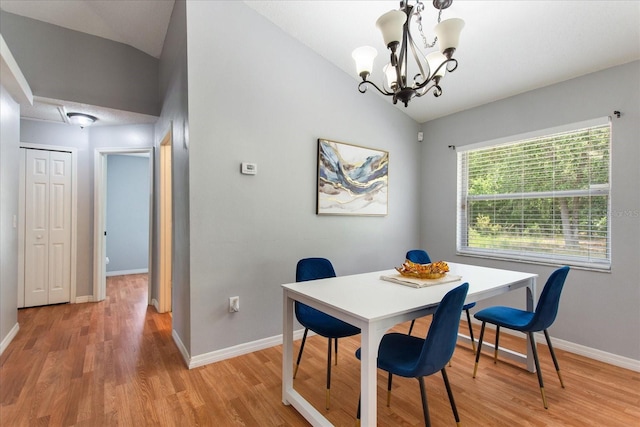 dining space with hardwood / wood-style floors, vaulted ceiling, and an inviting chandelier