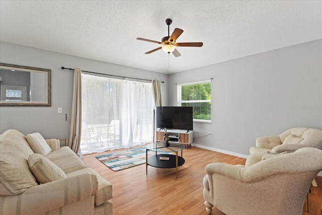 living room featuring ceiling fan, light wood-type flooring, and a textured ceiling