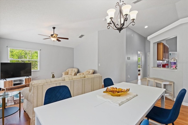 dining space with ceiling fan with notable chandelier, a textured ceiling, light wood-type flooring, and lofted ceiling