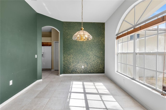 tiled empty room featuring a healthy amount of sunlight and a notable chandelier