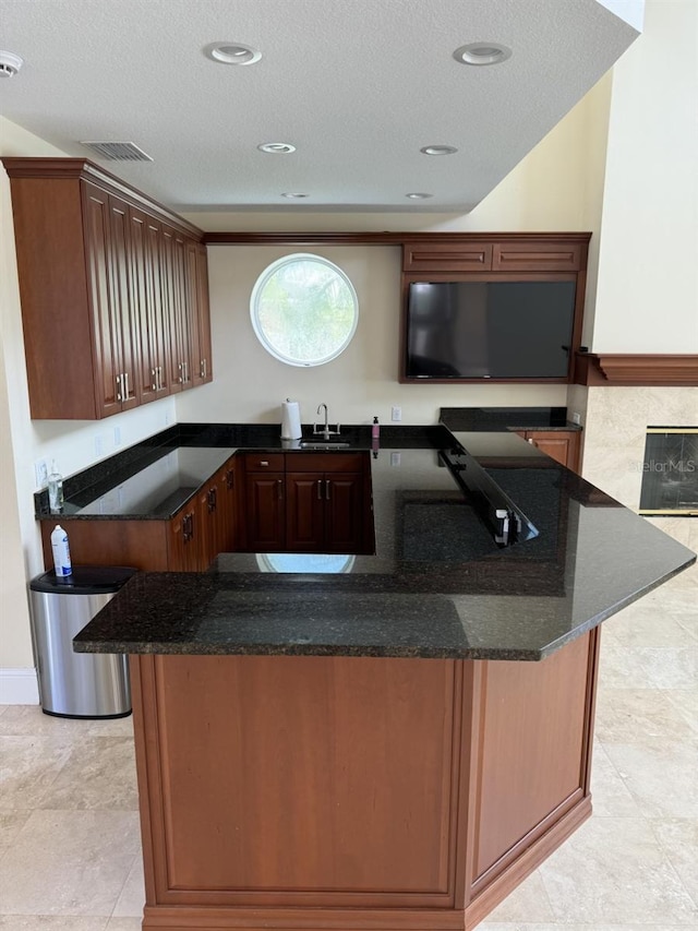 kitchen featuring kitchen peninsula, a textured ceiling, dark stone counters, and sink