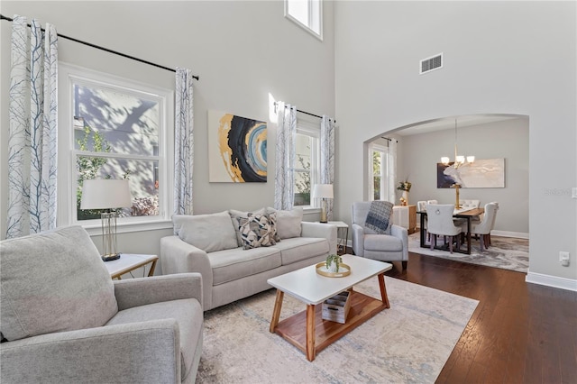 living room with a chandelier, a towering ceiling, plenty of natural light, and dark wood-type flooring