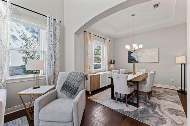 dining area featuring a chandelier, dark hardwood / wood-style flooring, and a raised ceiling