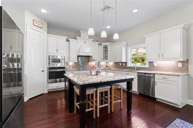 kitchen featuring light stone countertops, dark wood-type flooring, stainless steel appliances, a kitchen island, and white cabinets