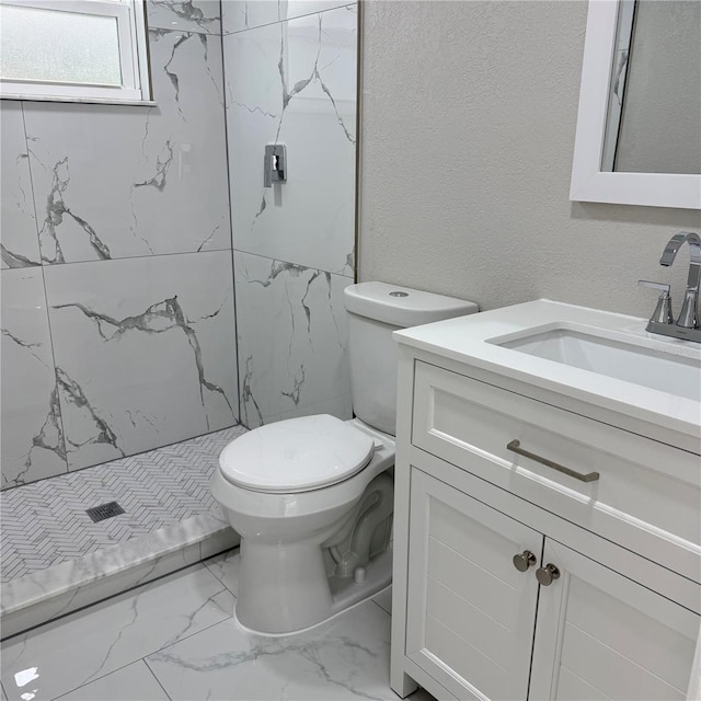 bathroom with a tile shower, vanity, and toilet