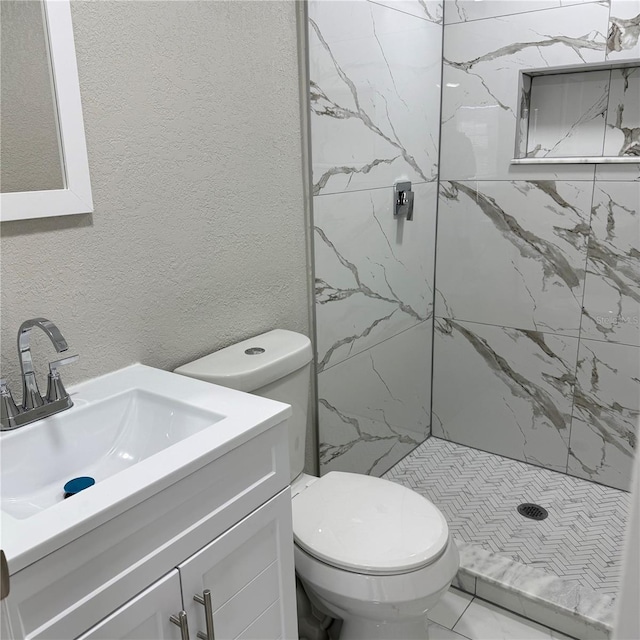 bathroom featuring a tile shower, vanity, and toilet