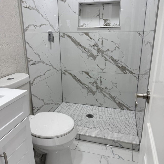 bathroom featuring a tile shower, vanity, and toilet