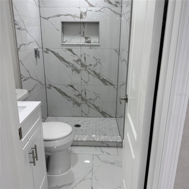 bathroom with tiled shower, vanity, and toilet