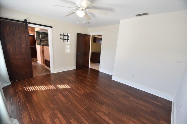 unfurnished room with a barn door, dark hardwood / wood-style floors, and ceiling fan