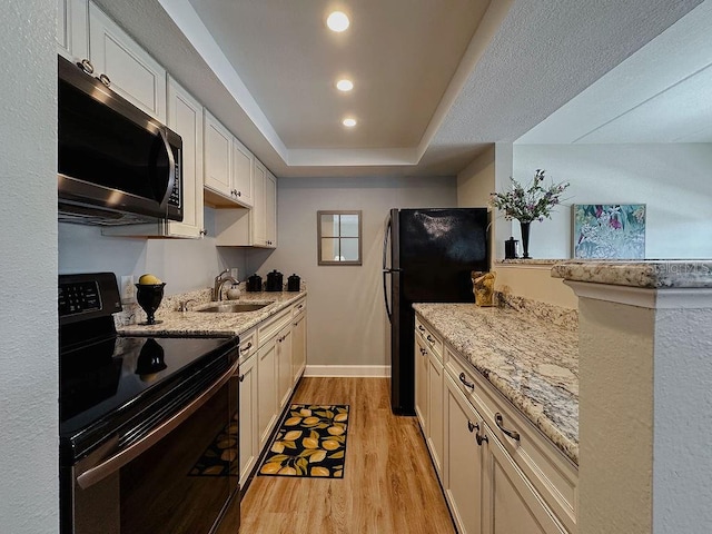 kitchen with white cabinetry, sink, black appliances, light stone countertops, and light wood-type flooring