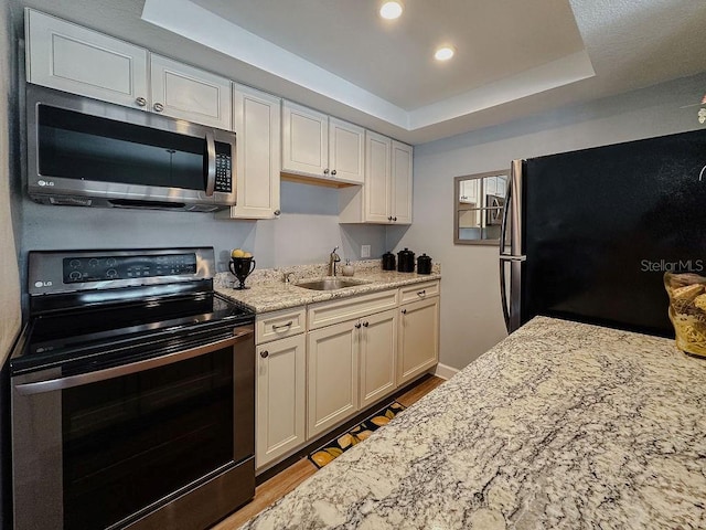 kitchen featuring stainless steel appliances, light hardwood / wood-style floors, sink, light stone counters, and a tray ceiling