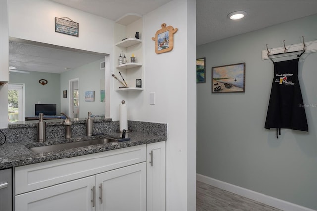 kitchen with white cabinetry, sink, dark stone counters, a textured ceiling, and light wood-type flooring