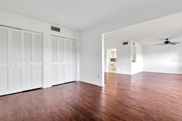 unfurnished bedroom featuring dark wood-type flooring, ceiling fan, and two closets