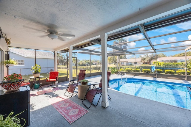 view of swimming pool with glass enclosure, a patio area, and ceiling fan