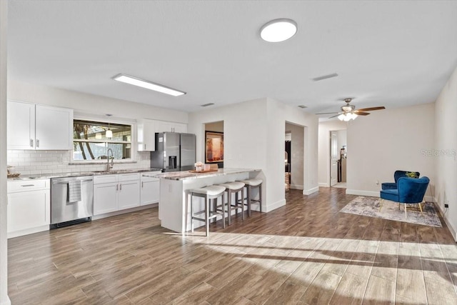 kitchen with white cabinetry, hardwood / wood-style floors, appliances with stainless steel finishes, and a kitchen breakfast bar