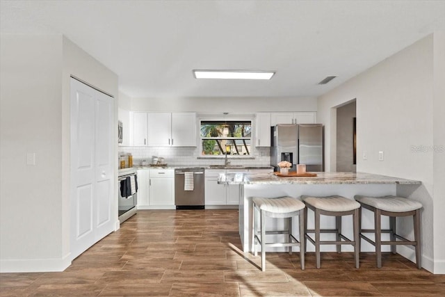 kitchen with kitchen peninsula, light stone counters, a kitchen breakfast bar, appliances with stainless steel finishes, and white cabinets