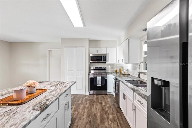 kitchen featuring sink, appliances with stainless steel finishes, hanging light fixtures, white cabinets, and dark wood-type flooring