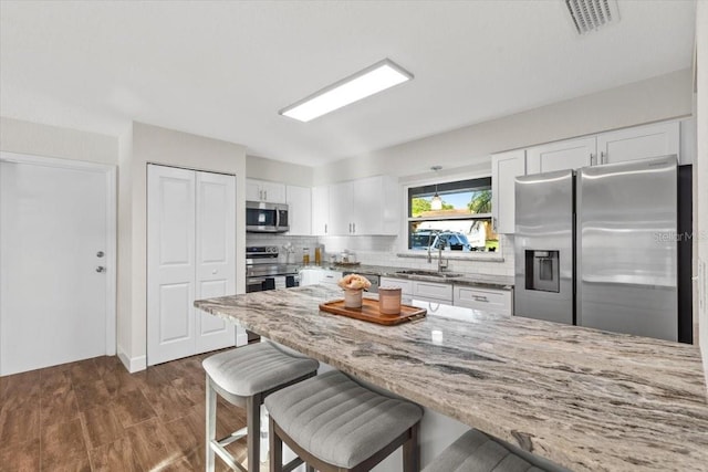 kitchen featuring sink, tasteful backsplash, light stone countertops, white cabinetry, and appliances with stainless steel finishes