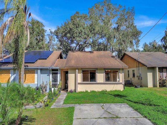 single story home featuring solar panels, cooling unit, and a front yard