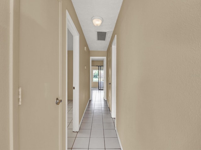 hall with a textured ceiling and light tile patterned flooring