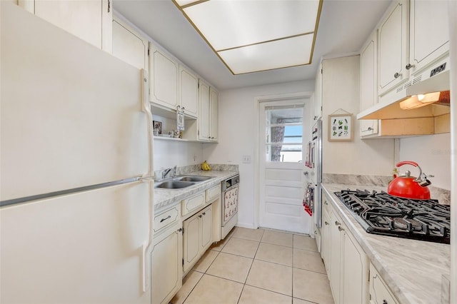 kitchen featuring stainless steel gas stovetop, white fridge, white cabinetry, and light tile patterned floors