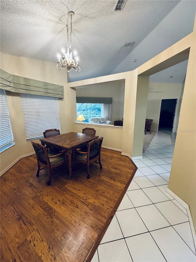 dining room featuring a chandelier, vaulted ceiling, a textured ceiling, and light hardwood / wood-style flooring