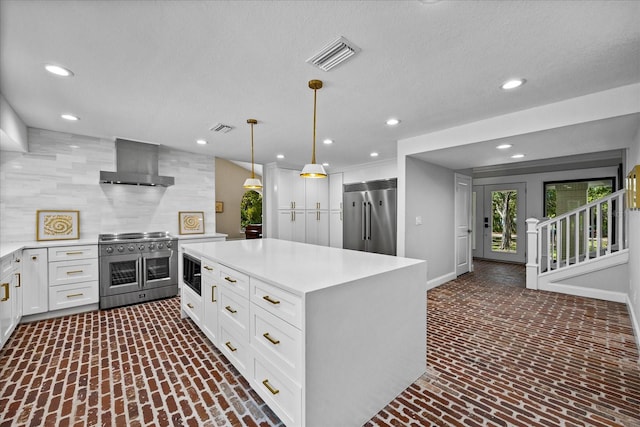 kitchen with white cabinetry, built in appliances, a kitchen island, pendant lighting, and wall chimney exhaust hood