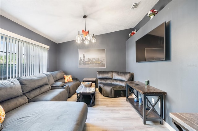 living room featuring an inviting chandelier, vaulted ceiling, and light hardwood / wood-style floors